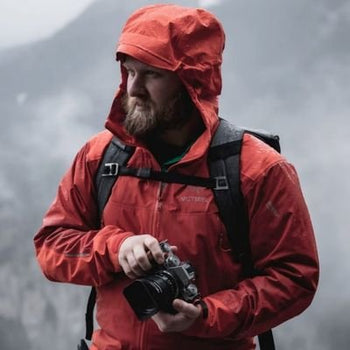 david lindahl in rain gear holding a camera and wearing a backpack